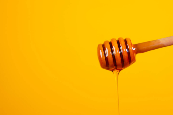 Στάγδην μέλι από κουτάλι σε κίτρινο φόντο - Φωτογραφία, εικόνα