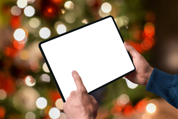 背後にあるクリスマスツリーのライトと手の中にタブレット。デザインプロモーションのための独立したディスプレイ。シーズンオンラインショッピングコンセプト - 写真・画像