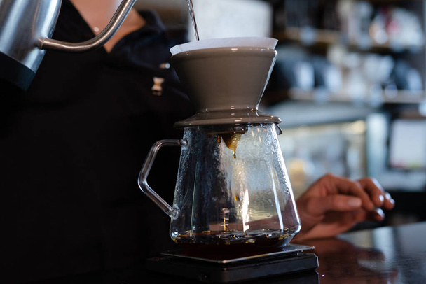 barista ρίχνουμε ζεστό νερό σε τραχύ καφέ φυσαλίδες καφέ μέσω φίλτρου στάγδην, σπίτι ζυθοποιίας διαδικασία. παρασκευή καφέ χρησιμοποιώντας chemex pour over καφετιέρα και βραστήρα στάγδην. Εναλλακτικοί τρόποι παρασκευής καφέ. - Φωτογραφία, εικόνα