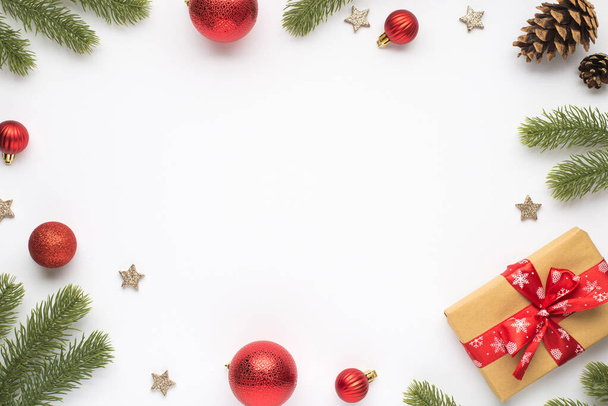 Foto von oben von Kiefernzweigen rote Weihnachtsbaumkugeln Kegel Sterne und Geschenkbox mit roter Schleife auf isoliertem weißem Hintergrund mit Leerstelle in der Mitte - Foto, Bild