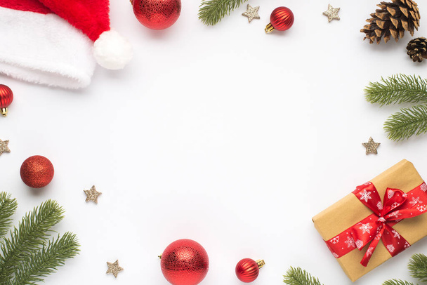 Bovenaanzicht foto van kerstman hoed dennen takken rood kerstboom ballen kegels sterren en geschenkdoos met rode strik op geïsoleerde witte achtergrond met lege ruimte in het midden - Foto, afbeelding