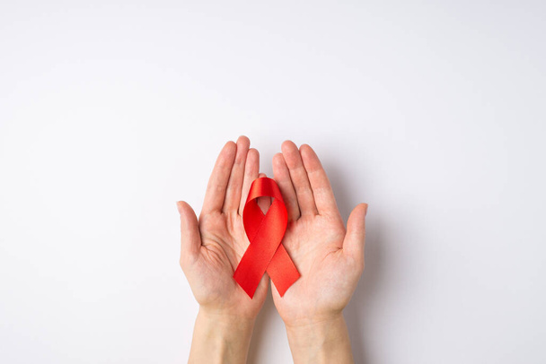 First person top view photo of hands holding red ribbon in palms symbol of aids awareness on isolated white background with copyspace - Photo, Image