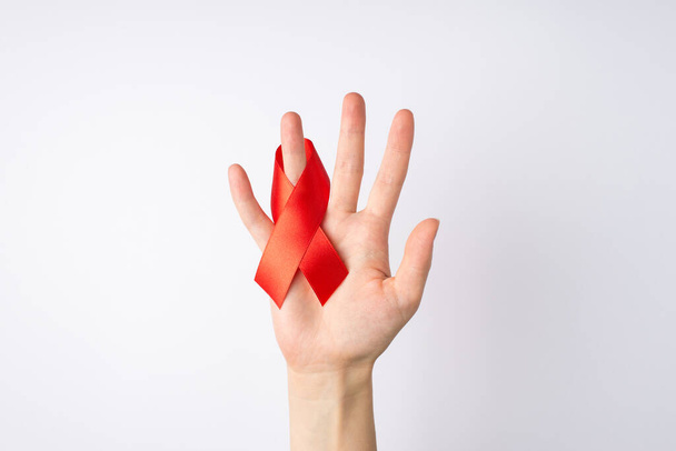 First person top view photo of female hand with red ribbon on ring finger symbol of aids awareness on isolated white background - Фото, зображення