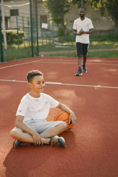 Multiracial boy sitting on a basketball court with a bottle of water - Zdjęcie, obraz