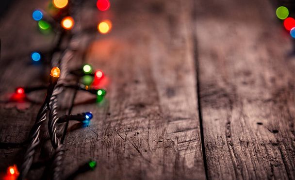 暗い古い風化したヴィンテージテーブルや木製の茶色のボード上のカラフルな電球のクリスマスの庭。クリスマスの装飾、大晦日。テキストの選択的焦点、ボケ、スペース. - 写真・画像