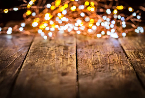 guirnalda de Navidad de luces blancas y doradas desenfocadas en mesa vintage envejecida oscura o tablero marrón de madera. Decoración de Navidad, Nochevieja. Enfoque selectivo, bokeh, espacio para texto. - Foto, imagen