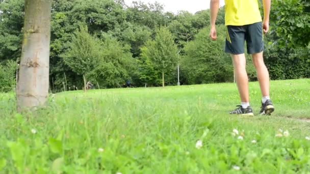 Man sports - running - man warming up and then start running - green grass with trees - other people in background - Footage, Video