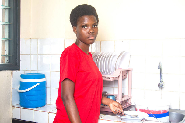 beautiful young girl wearing red t-shirt standing in the kitchen. - Фото, изображение