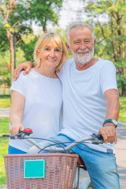 caucasian senior couple happy together riding bicycle outdoor in park in summer - Foto, imagen