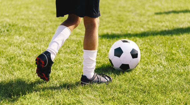 Fútbol corriendo con pelota en campo de hierba fresca. Boy in Cleats Kicking White and Black Soccer Ball (en inglés). Fondo horizontal de fútbol - Foto, Imagen