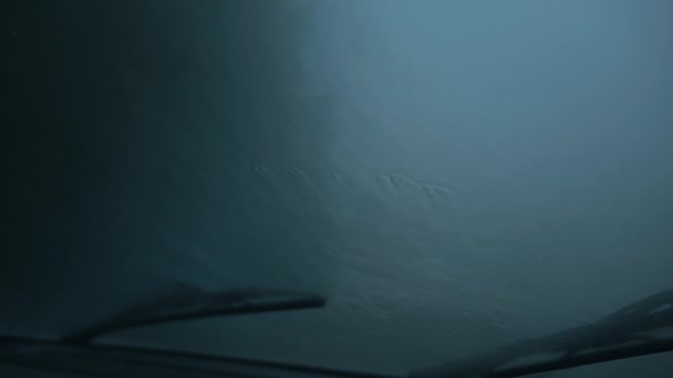 Primer plano de las corrientes de lluvia en el parabrisas y limpiaparabrisas en el vidrio contra un cielo gris desde el interior de un coche  - Metraje, vídeo