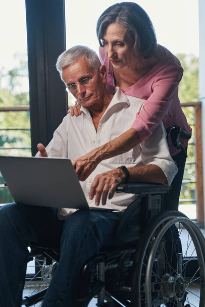 Aging female pointing at laptop screen of wheelchair user - Foto, immagini