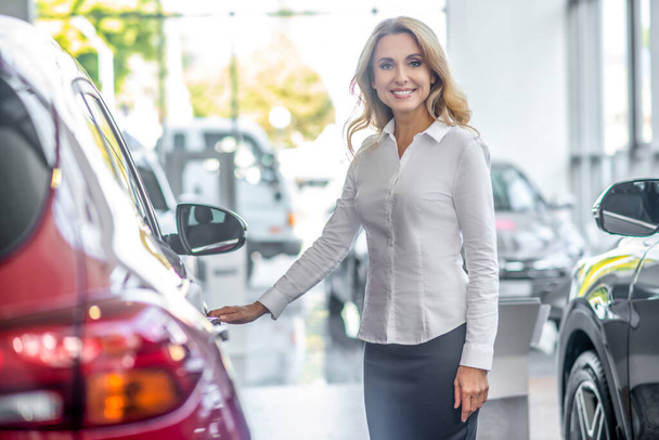 Smiling woman touching car door in dealership - Fotó, kép