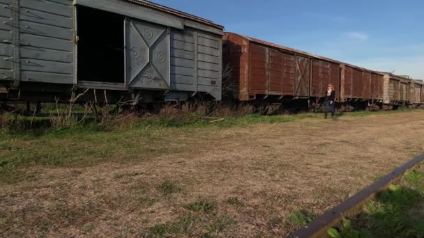 Mujer rubia adulta con gafas de sol caminando junto a un tren de carga abandonado. Concepto de lugares abandonados - Metraje, vídeo