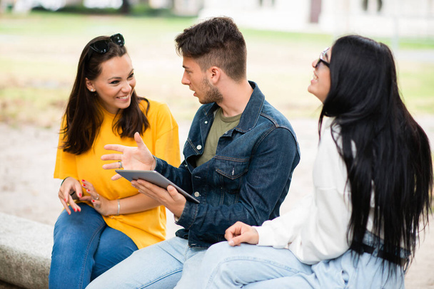 Three students studying together with a digital tablet sitting on a bench outdoor - Фото, зображення