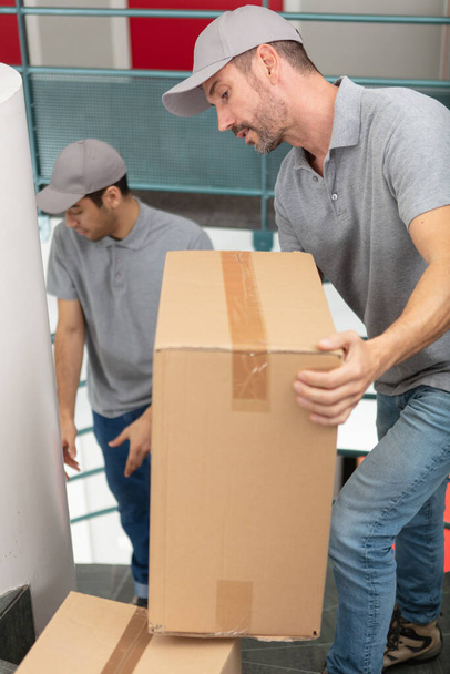 male movers carrying boxes up stairs in new house - 写真・画像