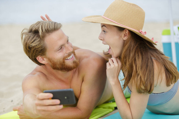 couple on beach woman making gesture while taking selfie - Zdjęcie, obraz