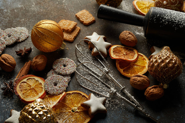 Festive biscuits, baking tools, toy ballsdry oranges, and nuts on the table; preparations for Christmas - Photo, Image