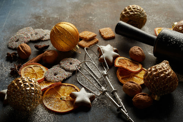 Cute composition with baking tools, baubles, dry oranges, biscuits, and nuts on the grunge surface - Photo, Image