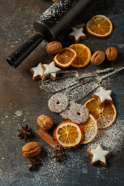 Вкусное рождественское печенье, сухие апельсины, орехи, сахарный порошок и хлебобулочные инструменты на столе - Фото, изображение