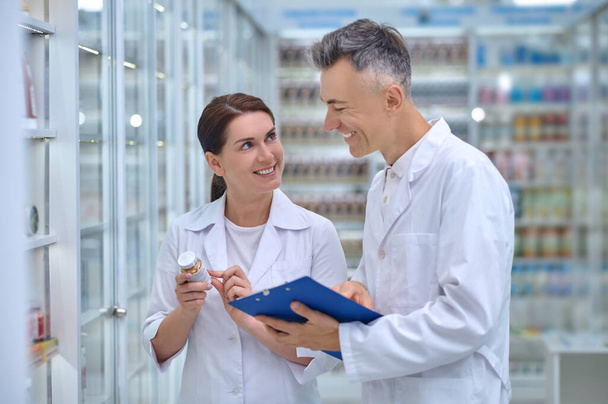 Woman with medicine and man with folder in pharmacy - Zdjęcie, obraz