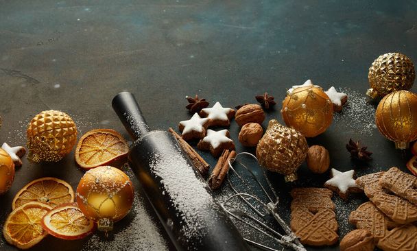 Festive Christmas cookies, baubles, dry oranges, cinnamon sticks, nuts, and baking tools on the table - Photo, image