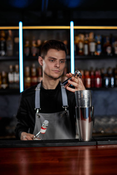 Bartender in apron adds ingredient to shaker - Фото, изображение