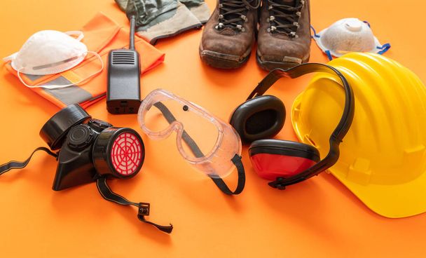 Arbeitskleidung Schutzausrüstung auf orangefarbenem Hintergrund, persönliche Schutzausrüstung. Gesundheits- und Sicherheitskonzept für Industriearbeiter auf der Baustelle. - Foto, Bild