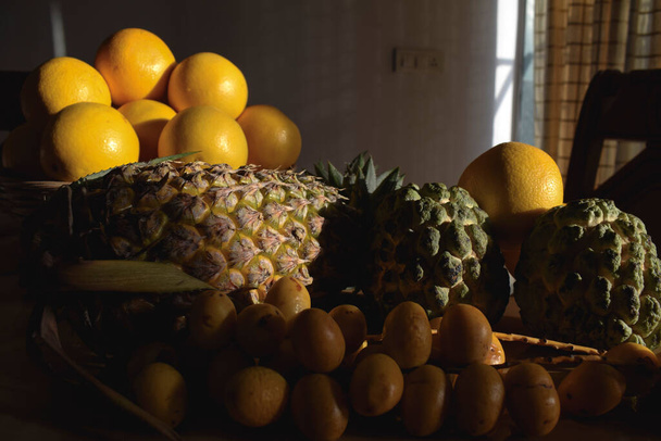 Różne owoce, takie jak ananas, malta, pomarańcze, jabłka z kremem, świeże żółte chrupiące daty na stole jadalnym na śniadanie. Stół w pomieszczeniach dieta jedzenie wiele owoców światło słoneczne - Zdjęcie, obraz