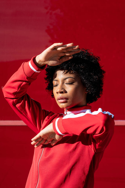 An African American female in red sport clothes standing on a red wall background - Zdjęcie, obraz