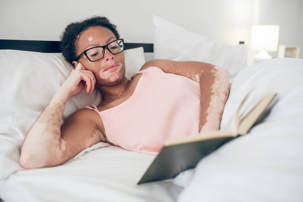 A young woman in eyeglasses reading a book while laying in bed - Foto, immagini
