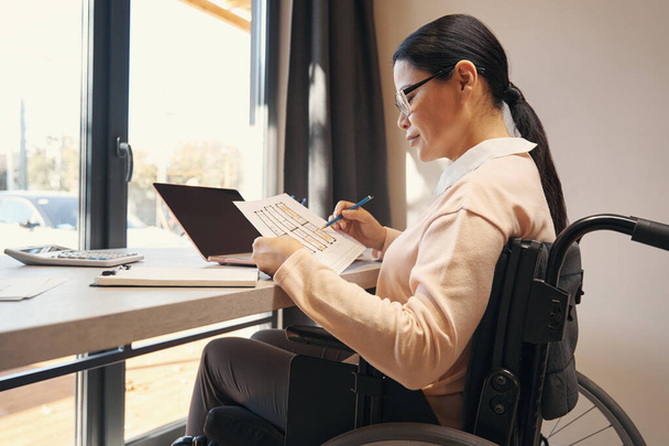 Mujer seria con discapacidad haciendo trabajo desde casa - Foto, imagen