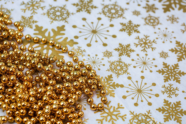 A closeup of golden Christmas bead decoration on snowflakes wallpaper background - Foto, afbeelding