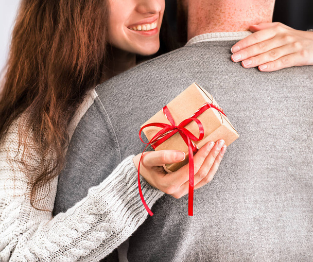 γυναίκα με ένα δώρο στο χέρι αγκαλιάζει έναν άντρα, κοντινό πλάνο - Φωτογραφία, εικόνα