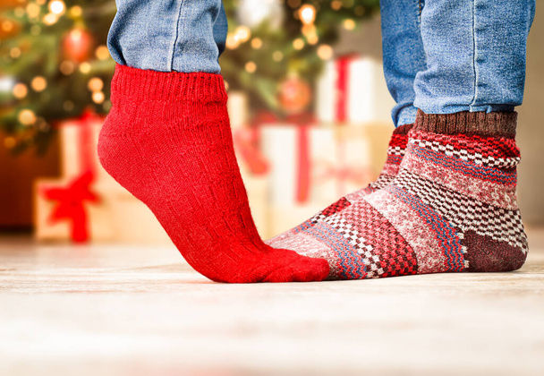 female and male feet in Christmas warm socks on the background of a Christmas tree with gifts - Fotoğraf, Görsel