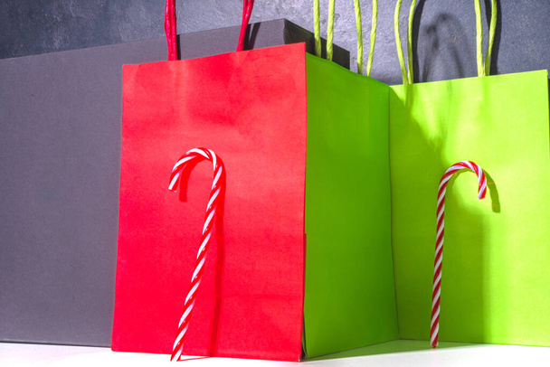 Απλή γραφιστική μοντέρνα Χριστουγεννιάτικη μακέτα με σκληρές σκιές. Γλυκά ζαχαροκάλαμου βασίζεται κάθετα σε κόκκινο πράσινο φόντο. Χαρτοσακούλες για ψώνια, Χριστούγεννα μαύρο Παρασκευή πώληση έννοια χώρο αντίγραφο - Φωτογραφία, εικόνα