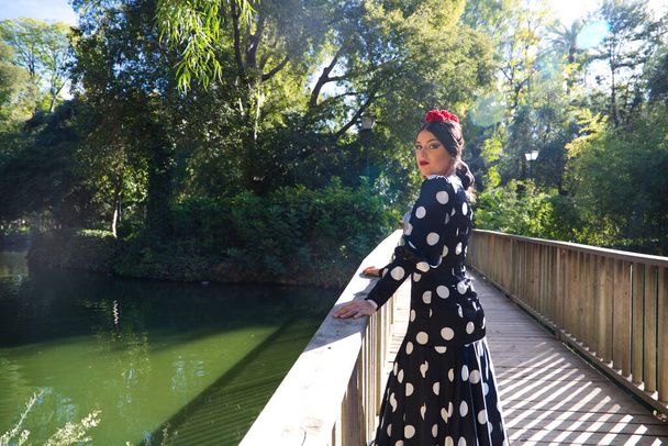bela espanhola morena dançarina flamenco mulher com um vestido típico flamenco com bolinhas brancas posando e olhando para a câmera em uma passarela de madeira. Património cultural flamenco da humanidade. - Foto, Imagem