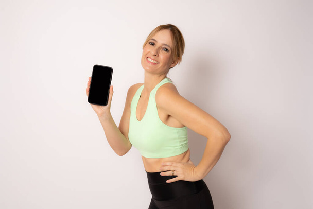 Giovane donna sportiva su sfondo bianco isolato che mostra il telefono cellulare. - Foto, immagini