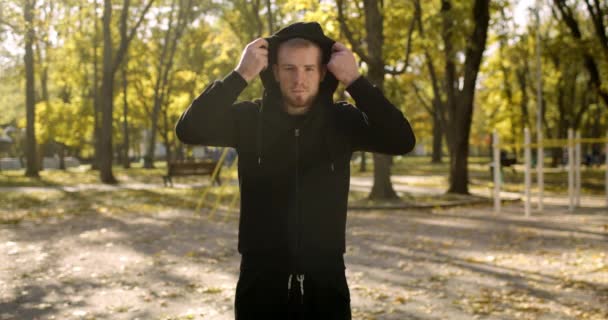 Mladý sportovní sebevědomý chlap oblékání kapotu svého sportovního obleku a pózování na kameru se založenýma rukama, zpomalený pohyb - Záběry, video