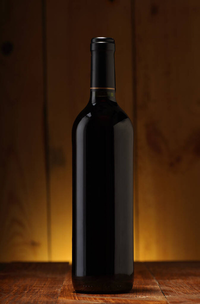 Flasche mit Rotwein auf dem Tisch und Hintergrund aus Holzbrettern - Foto, Bild