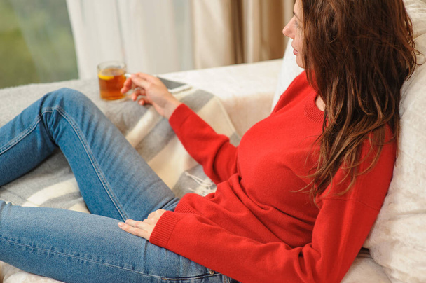 Mladá žena odpočívá na pohovce a drží šálek s citrónovým čajem. Žena snila v obývacím pokoji ležící na gauči. Žena přemýšlí, zatímco pije citrónový čaj doma. - Fotografie, Obrázek