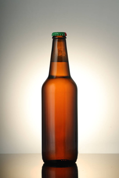 botella de cerveza marrón completa sobre fondo blanco con degradado y reflejo espejo - Foto, imagen