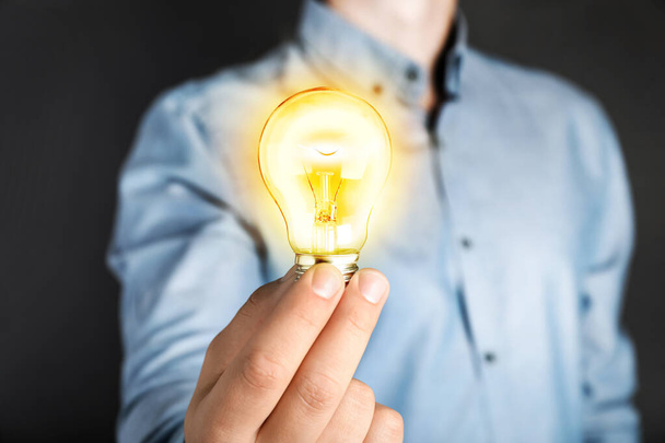 Glow up your ideas. Man holding light bulb on dark background, closeup - Φωτογραφία, εικόνα
