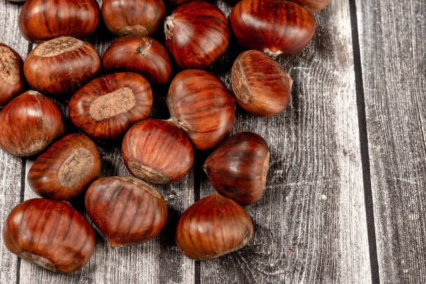 algunas castañas crudas, marron (Castanea sativa), una fruta clásica de otoño, sobre fondo rústico de madera de color claro. - Foto, Imagen