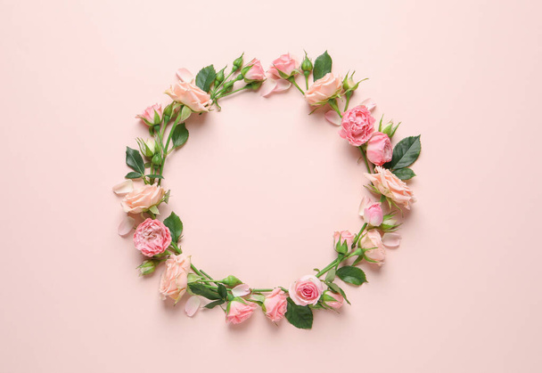Wreath made of beautiful flowers and green leaves on pale pink background, flat lay. Space for text - 写真・画像