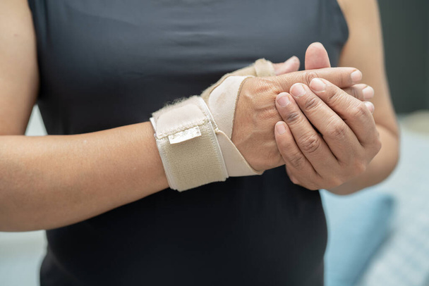 Asiatique femme d'âge moyen utilisent un bandage élastique pour traiter le syndrome De Quervain à la main et le doigt au bureau
. - Photo, image