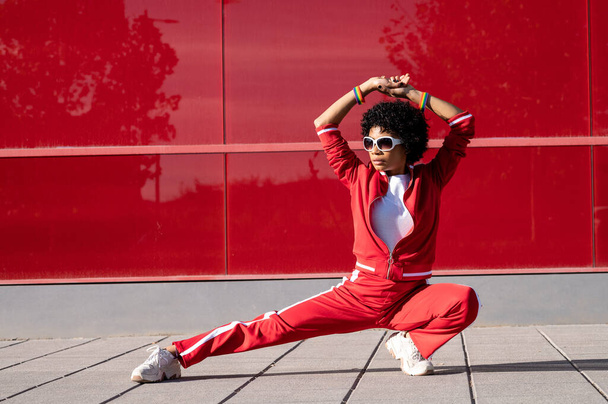 An African American female in red sport clothes in a hip hop pose on a red wall background - Foto, imagen