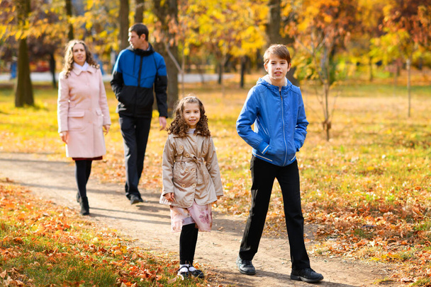 Familie wandelingen in het najaarspark langs het pad. Een prachtige natuur en bomen met gele bladeren. Helder zonlicht. - Foto, afbeelding