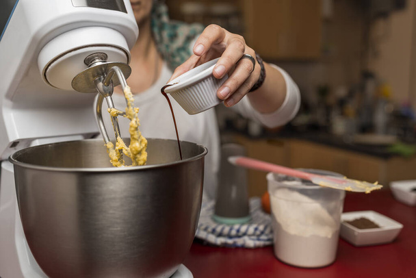 A woman putting vanilla extract in a mixer bowl to cook homemade Argentinian Alfajores - Foto, imagen