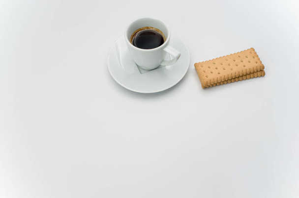 black hot ristretto coffee in a white stoneware cup with plate and biscuits on a white surface with text space - Fotografie, Obrázek